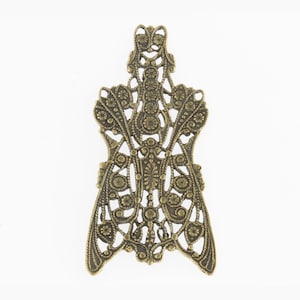 May include: A gold metal filigree design with a delicate, intricate pattern. The design is shaped like a butterfly with wings that are open and spread out.
