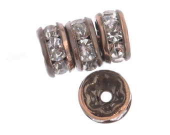 May include: Four copper-toned bead spacers with clear rhinestone accents. The spacers are round and have a hole in the center for stringing.