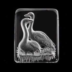 May include: A clear, rectangular glass piece featuring an engraved design of two swans. One swan is seated, and the other stands behind it. The swans are surrounded by detailed foliage, all set against a black background.