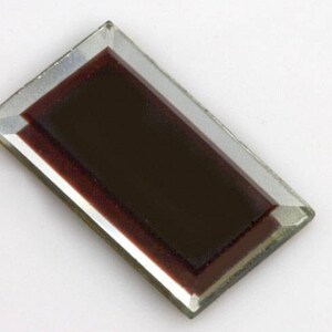 May include: A dark brown rectangular glass tile with beveled edges and a clear glass border.