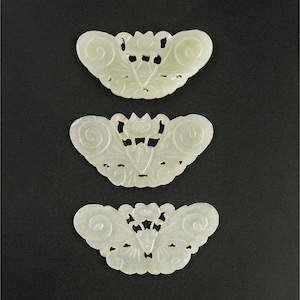 May include: Three white jade butterfly-shaped pendants with intricate carved designs. The pendants are arranged vertically, with the largest at the top and the smallest at the bottom.