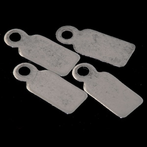 May include: Four silver metal tags with a hole at the top. The tags are rectangular and have a slightly textured surface.