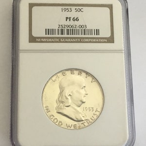 May include: A 1953 50C half dollar coin graded PF 66 by the Numismatic Guaranty Corporation. The coin is encased in a plastic slab with a white label.