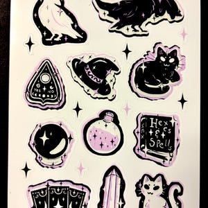 May include: A sheet of stickers featuring various mystical and witchy designs. Includes a ghost, raven, Ouija board, witch's hat, black cat, crystal ball, potion bottle, spell book, tarot cards, crystal, and a white cat. Each design has a black outline with a light purple fill.