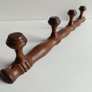 May include: A vintage wooden coat rack with four decorative knobs. The rack is made of dark brown wood and has a gently curved design. The knobs are round and have a detailed, layered appearance. A classic piece for entryways or bedrooms.
