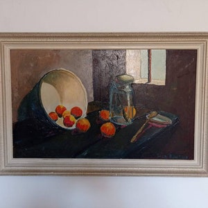 May include: A still life painting depicting a bowl of oranges, a glass jar, and a wooden spoon on a dark table. The painting is framed in a light wood frame.