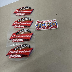 Puede incluir: Parches bordados con el logotipo de Budweiser y el texto "Atlanta Bud Bowl 2000", además de un gráfico de fútbol americano. Un parche dice "Budweiser 2000 All-Star Game". Los parches son rojos, blancos, marrones y azules.