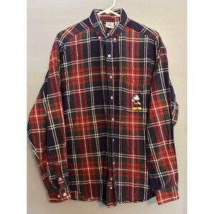 Puede incluir: Una camisa de manga larga con botones y un patrón de cuadros en rojo, azul marino y verde oscuro. La camisa incluye un cuello abotonado, un bolsillo en el pecho con un personaje de Mickey Mouse bordado y botones blancos al frente.
