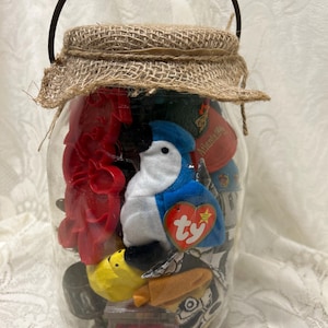 May include: A glass jar with a burlap lid and a metal handle filled with various small toys and trinkets, including a blue and white stuffed bird with a red "ty" tag.