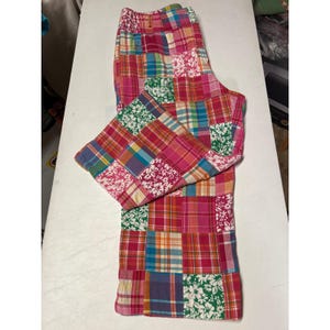 May include: A pair of pants featuring a colorful patchwork design composed of various fabric squares. The pattern includes a mix of plaid, checkered, and floral prints in shades of pink, blue, green, yellow, and white throughout the garment.
