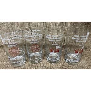 Puede incluir: Cuatro vasos de vidrio transparente con texto y gráficos blancos y rojos. Los vasos presentan el texto "Grand Royal Chapter" y "Grand Commandery Knights of Georgia". Los vasos están sobre una superficie de arpillera.