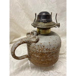 May include: A ceramic oil lamp with a handle. The lamp has a speckled gray and brown body with a metal top and a handle. The lamp is designed to look like a mug.