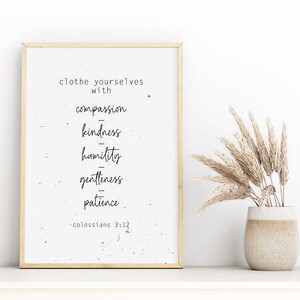 Peut inclure: Une affiche encadrée avec les mots "revêtez-vous de compassion, de bonté, d'humilité, de douceur, de patience" en écriture noire. Un vase avec des herbes séchées est à droite. Le cadre est brun clair.