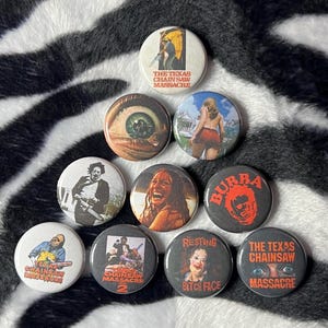 May include: A collection of ten circular pin-back buttons featuring various graphic designs related to The Texas Chain Saw Massacre horror film franchise, including character portraits, movie posters, and text such as Bubba and Resting Bitch Face.