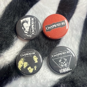 May include: Four Oxymoron band buttons. One button is red with the band's name. The other three are black with band member images and the band's name. One button has a skull and crossbones with the word "BEWARE".
