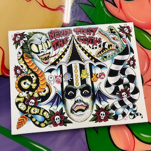 May include: A white card with a colorful illustration of a circus tent, a monster with fangs, a snake with skulls, and the text "Never Trust the Living".