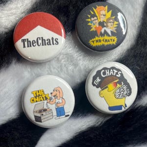 May include: Four round pinback buttons with different designs. One button has a red and white design with the text "The Chats". Another button has a cartoon image of a band. The other two buttons have cartoon images and the text "The Chats".