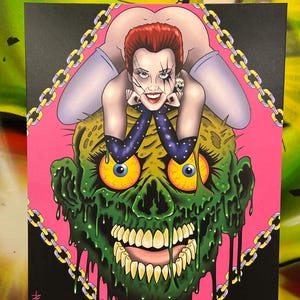 May include: A vibrant illustration featuring a woman with red hair and a skull earring, posed above a green zombie head. The artwork is framed by a pink background and a gold chain design. The artist's name, @BADFELLOW, is visible.