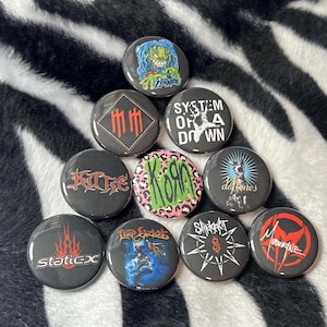 May include: A collection of nine circular pin-back buttons featuring various band logos and graphics, including Rob Zombie, Marilyn Manson, System of a Down, Kittie, Korn, Deftones, Static-X, Limp Bizkit, Slipknot, and Mudvayne, arranged in a pyramid.