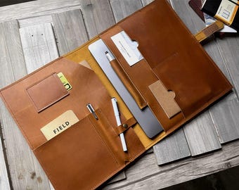 May include: A brown leather portfolio with multiple pockets and slots for holding pens, cards, and a laptop. The portfolio is open and has a notepad with the word "FIELD" written on it.