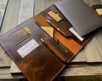 May include: A brown leather portfolio with a zipper closure, multiple pockets, and a pen holder. The portfolio is open to reveal a laptop, a notebook, and a pen.