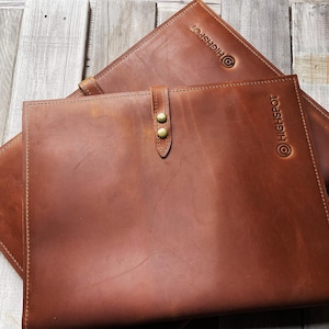 May include: Two brown leather document folders featuring a smooth finish and visible stitching along the edges. Each folder is embossed with the text HIGHSPOT and includes a central leather strap secured by two brass-colored metal snap buttons.