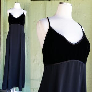 May include: A black evening gown with a velvet bodice and spaghetti straps. The bodice has a V-neckline and is trimmed with a thin black band. The skirt is a flowing, floor-length design. The dress is displayed on a mannequin.