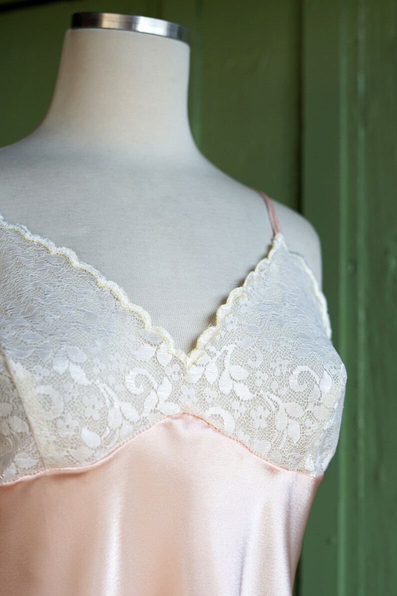 May include: A pink satin slip with white lace trim. The lace has a floral pattern.