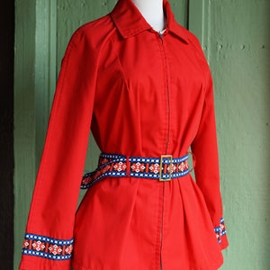 Puede incluir: Una chaqueta roja con cierre de cremallera y un cintur&oacute;n con estampado geom&eacute;trico. La chaqueta tiene mangas largas con un ribete con estampado geom&eacute;trico en los pu&ntilde;os.