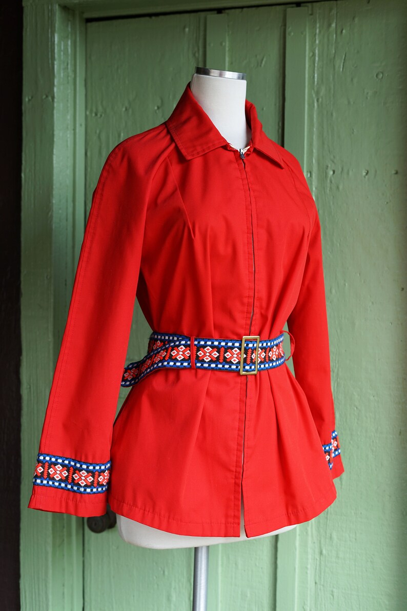 Puede incluir: Una chaqueta roja con cierre de cremallera y un cintur&oacute;n con estampado geom&eacute;trico. La chaqueta tiene mangas largas con un ribete con estampado geom&eacute;trico en los pu&ntilde;os.