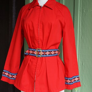 Puede incluir: Una chaqueta roja con cierre de cremallera y un cintur&oacute;n estampado. La chaqueta tiene ribetes azules y blancos en las mangas y una hebilla dorada en el cintur&oacute;n.