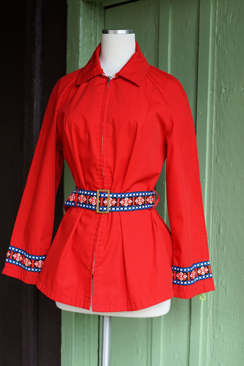 Puede incluir: Una chaqueta roja con cierre de cremallera y un cintur&oacute;n estampado. La chaqueta tiene ribetes azules y blancos en las mangas y una hebilla dorada en el cintur&oacute;n.