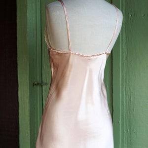 May include: A pale pink satin slip dress with thin straps. The dress is sleeveless and has a straight neckline.