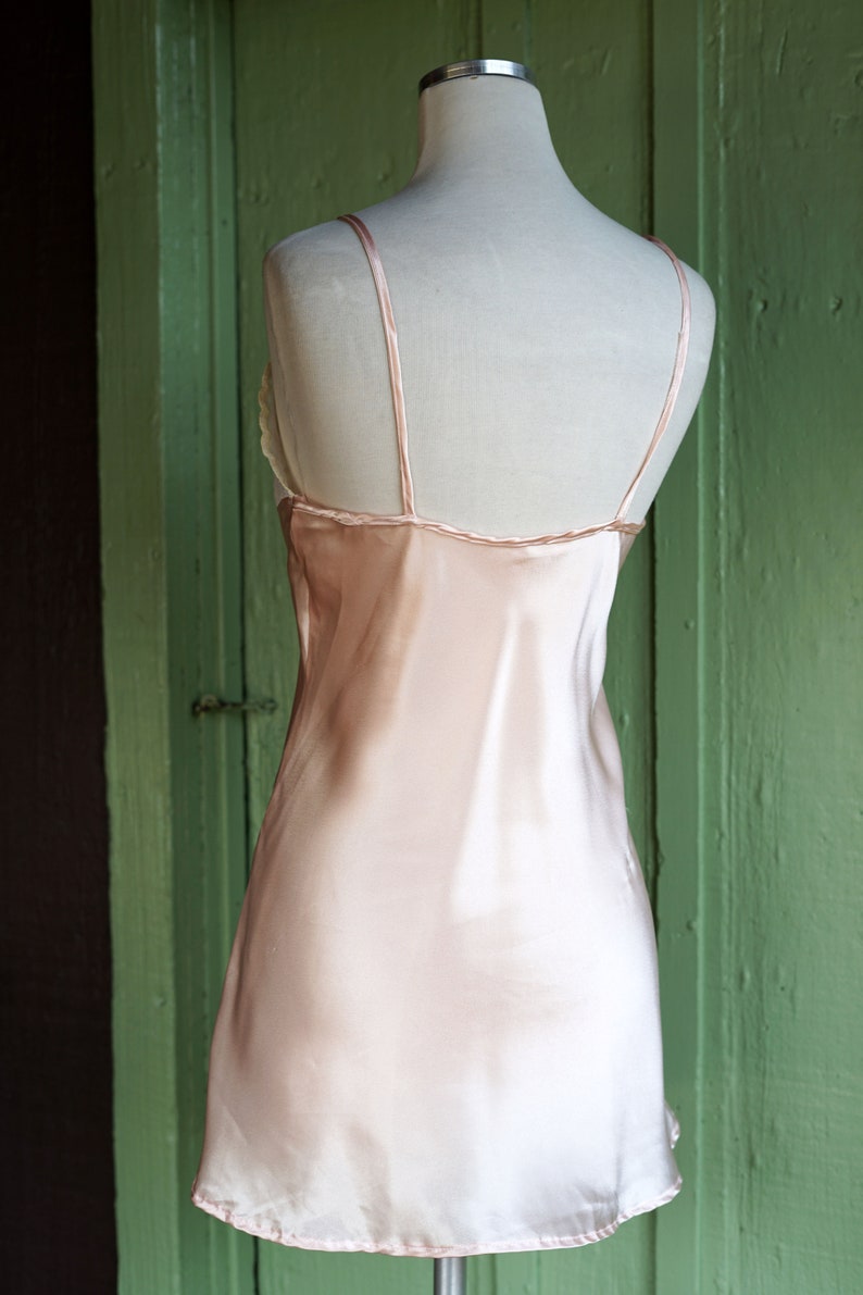 May include: A pale pink satin slip dress with thin straps. The dress is sleeveless and has a straight neckline.