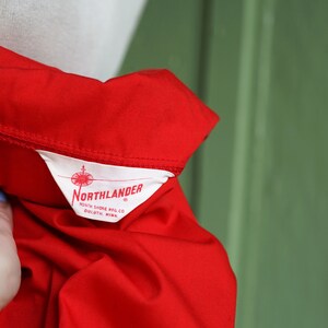 Puede incluir: Una camisa roja con una etiqueta blanca que dice "Northlander" North Shore Mfg. Co. Duluth, Minn.