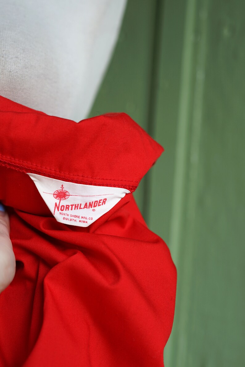 Puede incluir: Una camisa roja con una etiqueta blanca que dice "Northlander" North Shore Mfg. Co. Duluth, Minn.