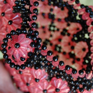 May include: A close-up of a pink and black beaded garland. The garland is made of small, round beads and is arranged in a circular pattern. The beads are strung together on a wire or thread.