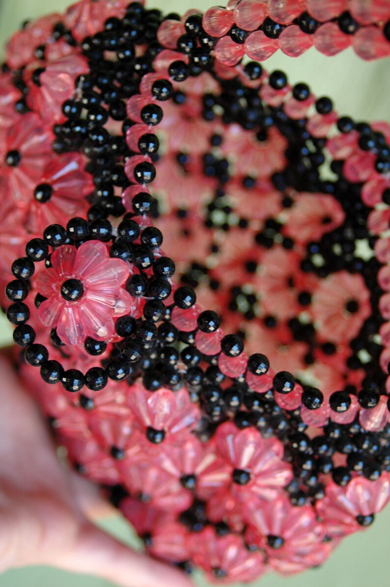 May include: A close-up of a pink and black beaded garland. The garland is made of small, round beads and is arranged in a circular pattern. The beads are strung together on a wire or thread.