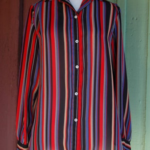 May include: A long-sleeved, striped button-down shirt in black, red, blue, and beige. The shirt is made of a sheer fabric and has a relaxed fit.