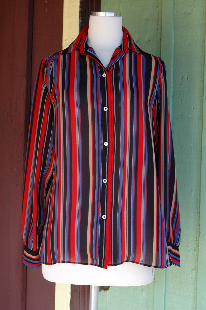 May include: A long-sleeved, striped button-down shirt in black, red, blue, and beige. The shirt is made of a sheer fabric and has a relaxed fit.