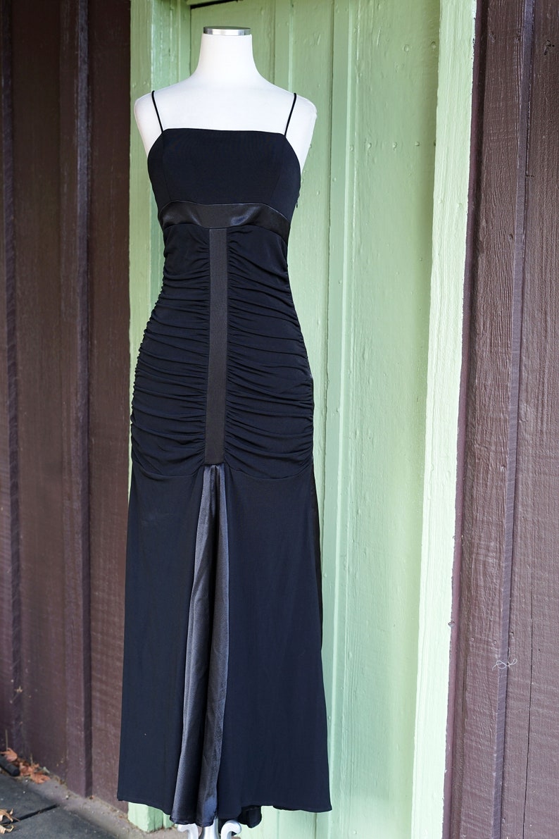 May include: A black, floor-length, sleeveless dress with a satin ribbon detail and a ruched bodice.
