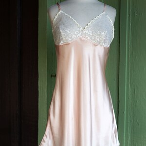 May include: A pale pink satin slip dress with a white lace bodice. The dress has thin straps and a flowing skirt.