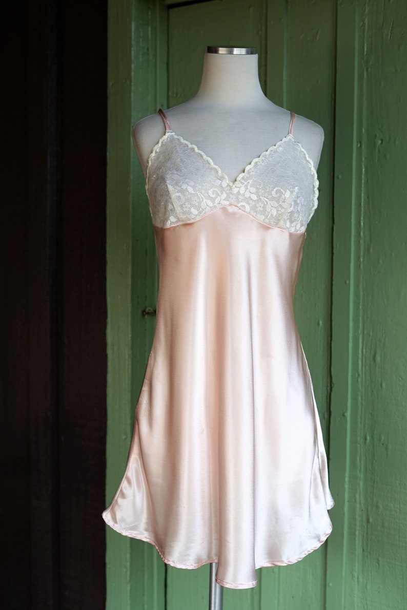 May include: A pale pink satin slip dress with a white lace bodice. The dress has thin straps and a flowing skirt.