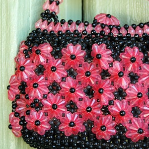 May include: A pink and black beaded handbag with a floral design. The bag is made of small, round beads that are strung together to create a pattern of flowers.
