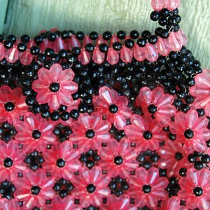 May include: A pink and black beaded purse with a flower pattern. The purse is made of small, round beads that are strung together to create a floral design.