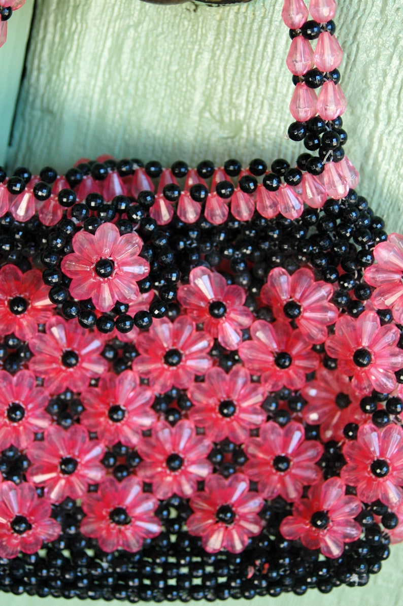 May include: A pink and black beaded purse with a flower pattern. The purse is made of small, round beads that are strung together to create a floral design.