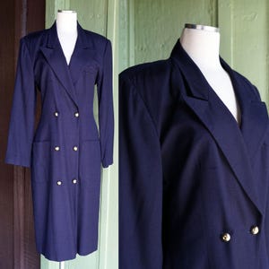 Puede incluir: Un vestido azul marino de doble botonadura con mangas largas y botones dorados. El vestido presenta una silueta entallada con cuello con solapas, bolsillos delanteros y un dobladillo a la rodilla. El vestido se exhibe en un maniquí.