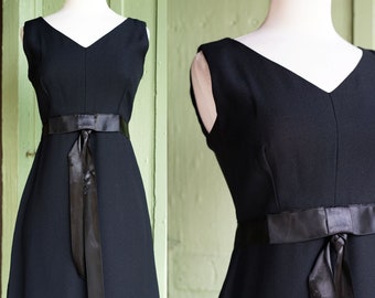 May include: A black sleeveless dress with a V-neckline and a black satin ribbon tied at the waist.