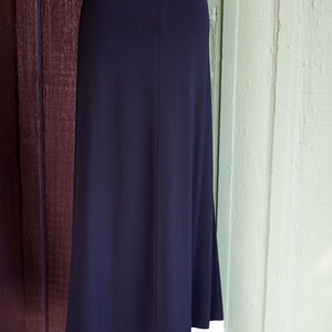 May include: A navy blue maxi skirt with a white hemline. The skirt has a simple, elegant design, with a straight silhouette and a contrasting white border at the bottom. The white border has a dotted pattern.