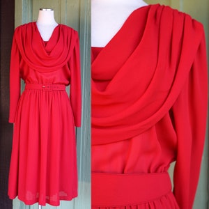 May include: A red dress with a cowl neck and a belt. The dress has long sleeves and a flowing skirt.